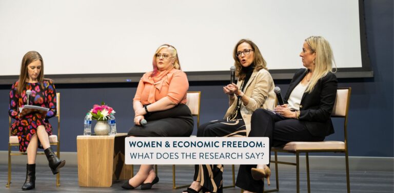 Color image of four women on a panel holding microphones with text in a blue box at the bottom of the screen that says "Women & Economic Freedom: What Does The research Say?".